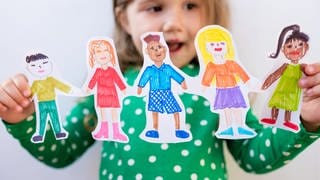 Ein Mädchen hält Papierkinder in der Hand. Heute ist Weltkindertag.