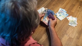 Eine ältere Frau zählt Geld an einem Tisch. Wo geht das Geld aus meinen Steuern hin? Was macht Rheinland-Pfalz damit? Ein FAQ gibt einen Überblick.