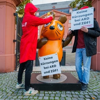 Die Figur der Maus aus der "Sendung mit der Maus" steht zwischen Aktivisten von Campact vor dem Landtag Rheinland-Pfalz.