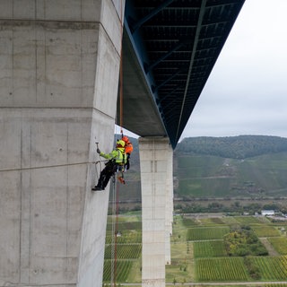 Industriekletterer seilen sich an einem Pfeiler der Hochmoselbrücke ab. Sie prüfen, ob es Schäden gibt. Zuständig für das Prüfen von Straßen und Brücken in RLP ist der Landesbetrieb Mobilität.