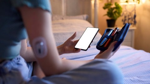 Diabetespatientin mit Handy, Messgerät und Insulinspritze zuhause - Über die ePA sollen wichtige Patienten-Informationen immer schnell verfügbar sein.