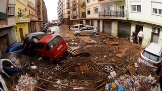 Von den Wassermassen der Überschwemmungen übereinander geschobene Autos liegen in einer überfluteten Straße in Spanien.