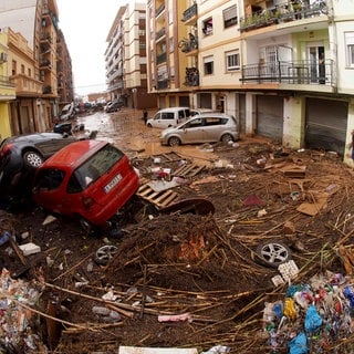 Von den Wassermassen der Überschwemmungen übereinander geschobene Autos liegen in einer überfluteten Straße in Spanien.