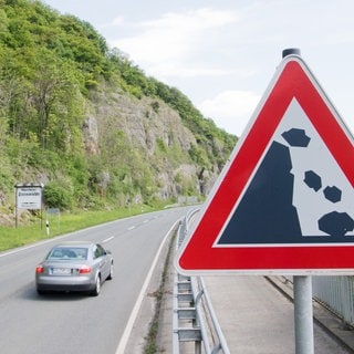 Ein Auto fährt über eine Straße, vorbei an Felsen - in Bingen Büdesheim stürzten Felsbrocken auf Autos