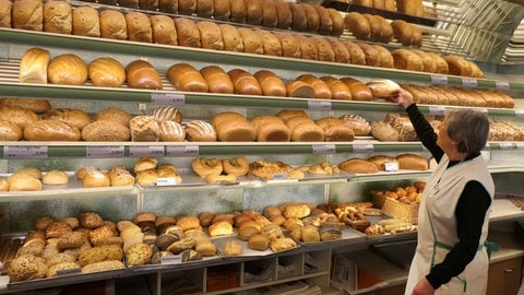 Eine Bäckereiverkäuferin mit grauem Haar holt Brot aus dem Verkaufsregal. Wenn die Boomer in Rente gehen, werden in mehr als der Hälfte der Berufe in RLP Arbeitskräfte fehlen.