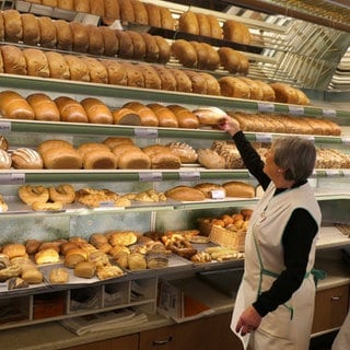 Eine Bäckereiverkäuferin mit grauem Haar holt Brot aus dem Verkaufsregal. Wenn die Boomer in Rente gehen, werden in mehr als der Hälfte der Berufe in RLP Arbeitskräfte fehlen.