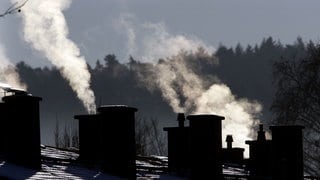 Rauchende Schornsteine auf schneebedecktem Dach (Symbolbild). In Rheinland-Pfalz heizen die meisten mit Gas und Öl.