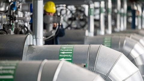 Ein Mitarbeiter kontrolliert Fernwärmeleitungen in einem Kraftwerk (Symbolbild). In Rheinland-Pfalz sollen künftig mehr Heizungen an Fernwärmenetze angebunden werden.