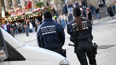 Ein Polizist und eine Polizistin stehen vor ihrem Einsatzwagen vor einem Weihnachtsmarkt. Nach dem tödlichen Anschlag auf dem Weihnachtsmarkt in Magdeburg wird bundesweit die Präsenz der Polizei auf Weihnachtsmärkten erhöht, auch in Rheinland-Pfalz.