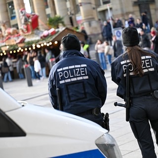 Ein Polizist und eine Polizistin stehen vor ihrem Einsatzwagen vor einem Weihnachtsmarkt. Nach dem tödlichen Anschlag auf dem Weihnachtsmarkt in Magdeburg wird bundesweit die Präsenz der Polizei auf Weihnachtsmärkten erhöht, auch in Rheinland-Pfalz.