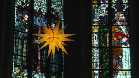 Ein gelber Weihnachtsstern vor den bunten Fenstern der Gedächtniskirche in Speyer. Hier predigte Kirchenpräsidentin Dorothee Wüst am ersten Feiertag davon, dass Weihnachten gegen Furcht hilft.