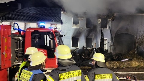 Einsatzkräfte stehen bei den Löscharbeiten in Hockweiler im Kreis Trier-Saarburg vor der Brandruine eines Wohnhauses. 