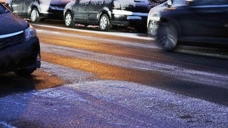 Autos mit Reif an den Reifen stehen auf einer eisglatten Straße. Mit Rutschgefahr geht 2024 in Rheinland-Pfalz zu Ende.