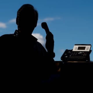 Ein Mann steht vor einem Fenster und hält ein Telefon in der Hand.
