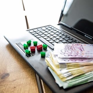 Kleine Häuser und geldscheine liegen auf Computer - Mann aus Kaiserslautern wird bei Immobilie im Internet betrogen