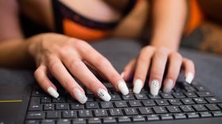 Eine Frau mit lackierten Nägeln tippt auf einem Computer. 