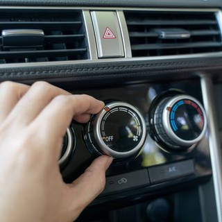 Eine Klimaanlage in einem Auto, eine Hand dreht am Regler.