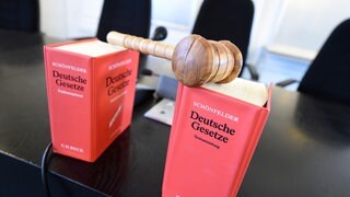 Auf einer Richterbank stehen zwei Bücher mit Deutschen Gesetzen, darauf liegt ein Richterhammer aus Holz