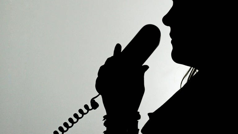 Polizei Kaiserslautern registriert zahlreiche Schockanrufe - eine Frau im Schatten hält einen Telefonhörer