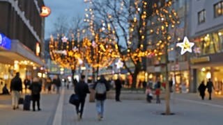 Menschen gehen in der Vorweihnachtszeit in einer Fußgängerzone einkaufen.