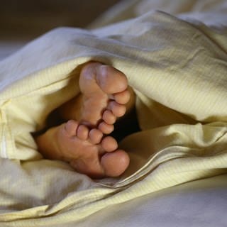 Die Füße einer Frau ragen unter einer Bettdecke hervor. 