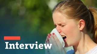 Eine Frau mit Allergie niest in ein Taschentusch - Interview zum Thema Heuschnupfen