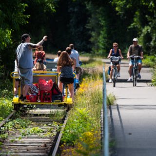 Draisinenstrecke im Glantal wieder voll befahrbar - Menschen fahren auf einer Draisine an Fahrradfahrern vorbei