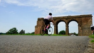 Der Zellertalradweg ist bei Radfahrerinnen und Radfahrern beliebt. Er ist einer von vielen Radwegen im Donnersbergkreis. Im Hintergrund ist der Brückentorso in Marnheim zu sehen.