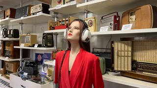 Frau mit Kopfhörer steht vor mehreren alten Radios - 100 Jahre Radio im Radiomuseum in Obermoschel