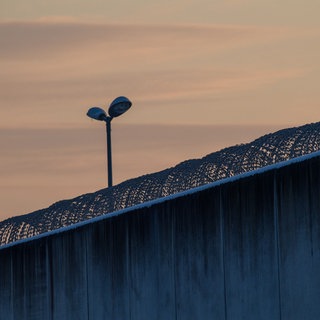 Die dicke Mauer eines Gefängnisses mit Stacheldraht.