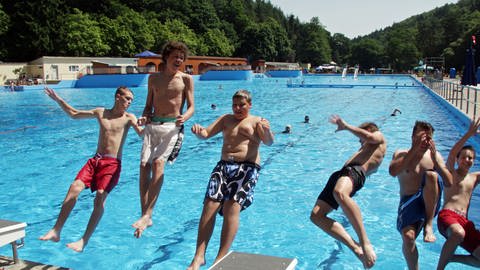 Sechs junge Männer springen rückwärts in das Becken eines Freibades 