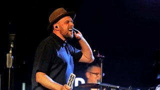 Sänger steht vor Orchester und hält sich die Hand ans Ohr - Max Mutzke singt mit der SWR Big Band bei "Euroclassic"-Festival 