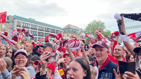 FCK-Fans feiern Mannschaft auf dem Stiftsplatz trotz Regen in Kaiserslautern.