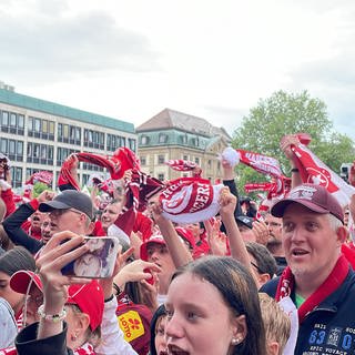 FCK-Fans feiern Mannschaft auf dem Stiftsplatz trotz Regen in Kaiserslautern.