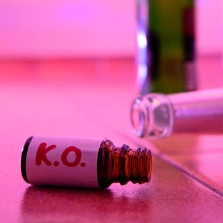 Ein kleines Fläschchen mit der Aufschrift "K.O." liegt neben mehreren Flaschen alkoholischer Getränke.