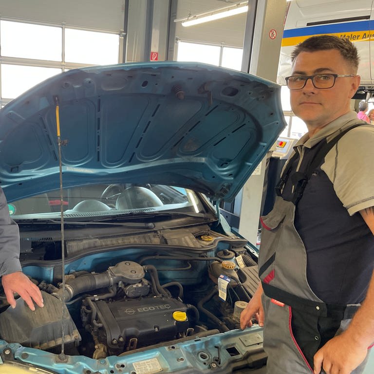 Zwei Männer stehen an einem Auto mit offener Motorhaube - Geflüchteter aus der Ukraine arbeitet in Autowerkstatt in Weilerbach