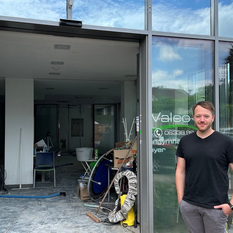 Florian Meyer, der Inhaber der Physiopraxis in Hornbach, steht vor seiner Praxis. Durch die offene Glastür sieht man die zerstörten Räume. (SWR)
