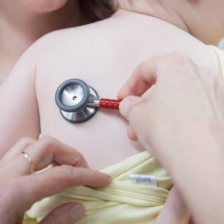 Ein kleines Kind wird am Rücken von einem Arzt mit dem Stethoskop abgehört 