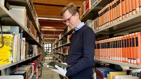 Andreas Rosteck, Leiter der Uni-Bibliothek in Kaiserslautern hält ein altes Buch in der Hand. Bücher aus dem 19. Jahrhundert könnten mit Arsen belastet sein.