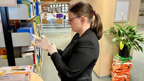 Carina Heisel von der Uni-Bibliothek in Kaiserslautern hält ein altes Buch in der Hand. Bücher aus dem 19. Jahrhundert könnten mit Arsen belastet sein.