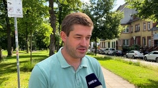 Patrick Schäfer, Fraktionsvorsitzender der SPD im Kaiserslauterer Stadtrat, steht da und spricht ins Mikrofon, hinter ihm der Stadtpark in Kaiserslautern. (SWR)