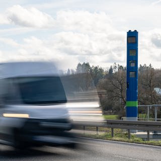 Ein Bild zeigt eine blaue Stehle zur Erfassung der Lkw-Maut auf einer Landstraße, ein Transporter fährt daran vorbei. (IMAGO)