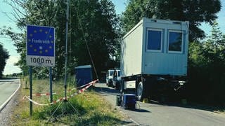 Grenzübergang zu Frankreich bei Hornbach in der Südwestpfalz ist zu sehen. Im Hintergrund neben der Straße zwei Polizeiautos und ein Container.