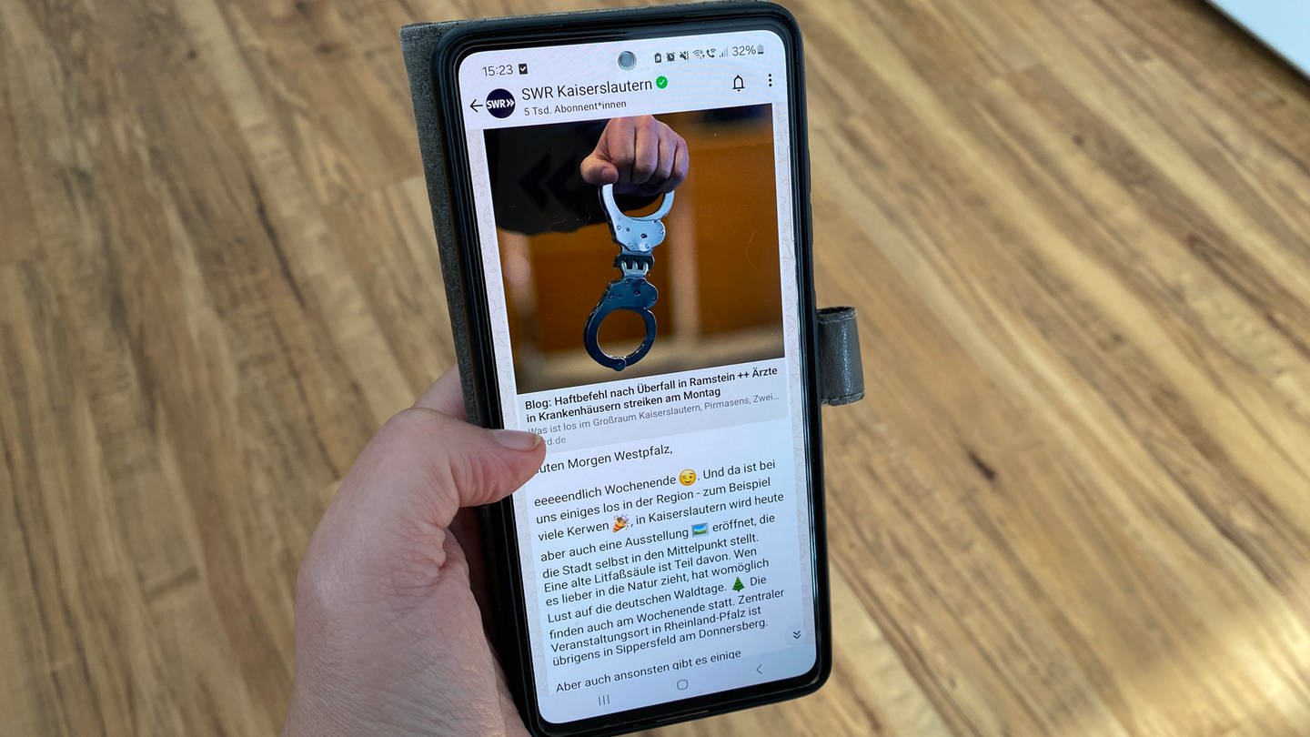 Eine Frau hält ein Smartphone in der Hand, darauf ist der WhatsApp-Kanal des SWR Kaiserslautern zu sehen.