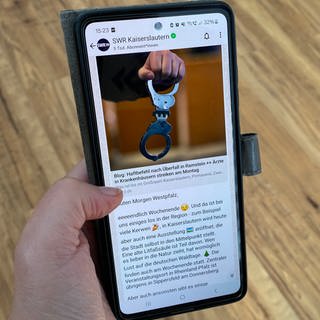 Eine Frau hält ein Smartphone in der Hand, darauf ist der WhatsApp-Kanal des SWR Kaiserslautern zu sehen.