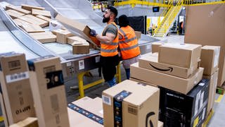 Männer stehen an einer Rutsche, wo Pakete von Amazon ankommen - in Zweibrücken entsteht für drei Monate ein Sortierzentrum