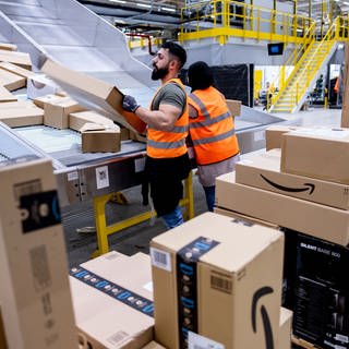 Männer stehen an einer Rutsche, wo Pakete von Amazon ankommen - in Zweibrücken entsteht für drei Monate ein Sortierzentrum