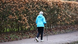 Seniorin geht mit Stöcken spazieren.