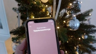 Mit einem Smartphone wird die Nummer der Telefonseelsorge vor einem Weihnachtsbaum gewählt. 