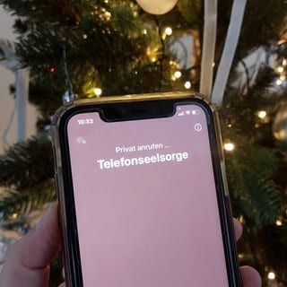 Mit einem Smartphone wird die Nummer der Telefonseelsorge vor einem Weihnachtsbaum gewählt. 